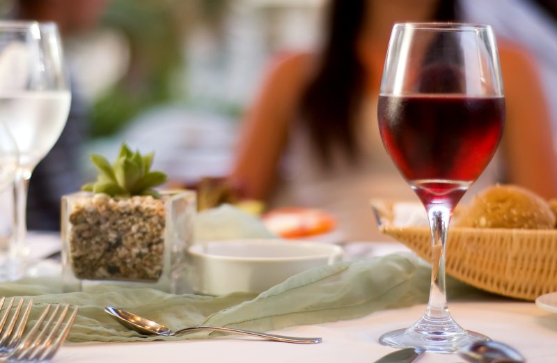 Gedeckter Restauranttisch mit einem Glas Rotwein im Vordergrund