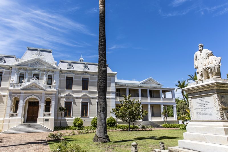 Historisches weißes Universitätsgebäude mit Palme und Denkmal davor